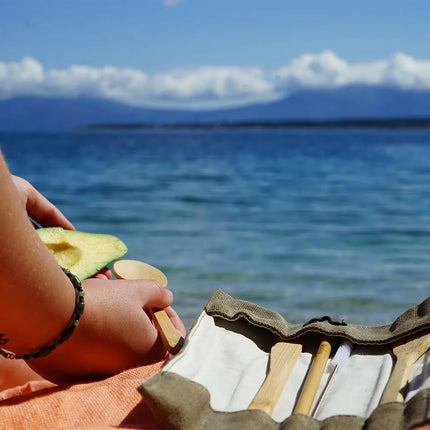 Persoon die buiten aan zee eet met een bamboe bestekset van Bambaw in een stoffen etui, als sfeerbeeld van gebruik onderweg.