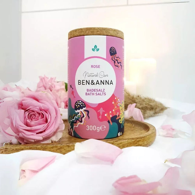 Ben & Anna badzout roos in een papieren koker met kurkdeksel, omringd door rozenblaadjes op een houten tray