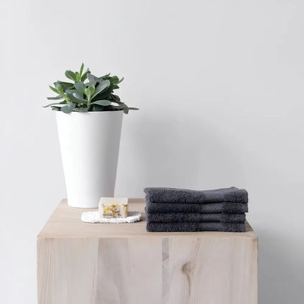 Stapel antracietkleurige Bo Weevil gezichtsdoekjes op een houten kast naast een plant en zeep