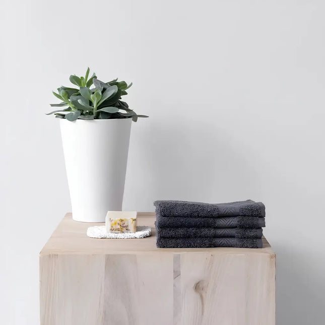 Stapel antracietkleurige Bo Weevil gezichtsdoekjes op een houten kast naast een plant en zeep