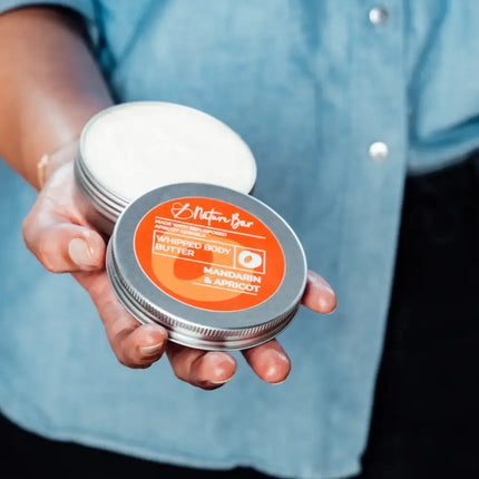 Hand houdt een blikje whipped body butter mandarijn‑abrikoos vast