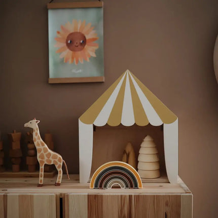 Sfeerbeeld van de Mushie Regenboog Stapeltoren in een kinderkamer, voor een geel-wit circustentje op een houten kastje