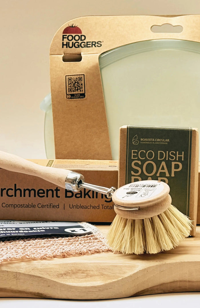 Duurzame keukenproducten op een houten plank, waaronder Food Huggers, bakpapier, afwasborstel, eco afwaszeep en schoonmaakdoekje.
