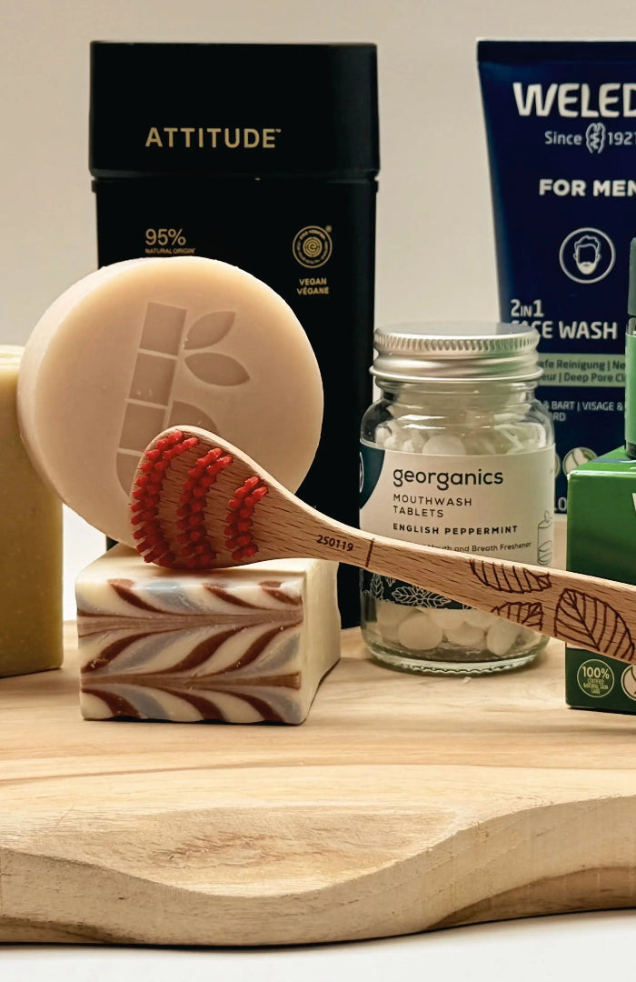 Duurzame verzorgingsproducten op een houten plank, waaronder zeep, Weleda Skin Food, Georganics en een houten tongschraper.