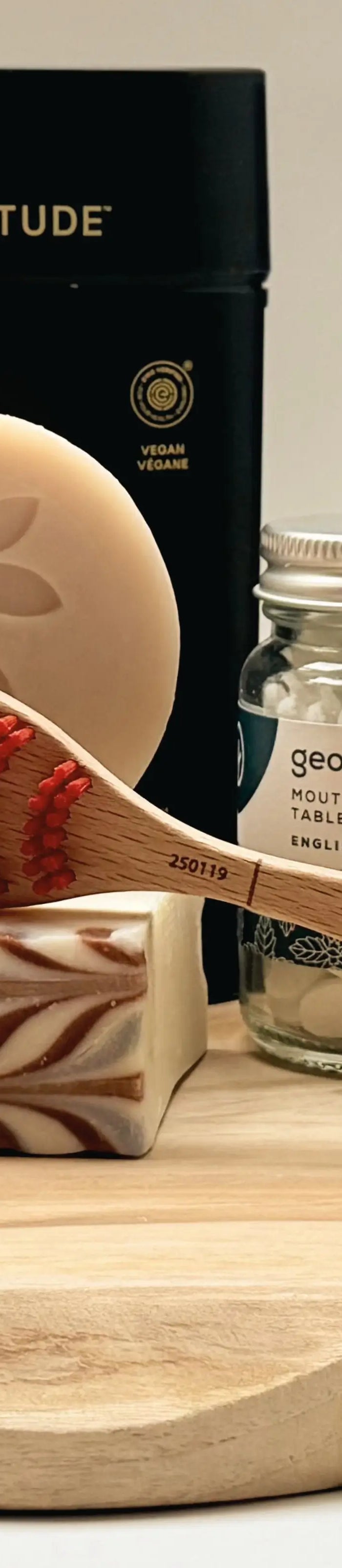 Duurzame verzorgingsproducten op een houten plank, waaronder zeep, Weleda Skin Food, Georganics en een houten tongschraper.