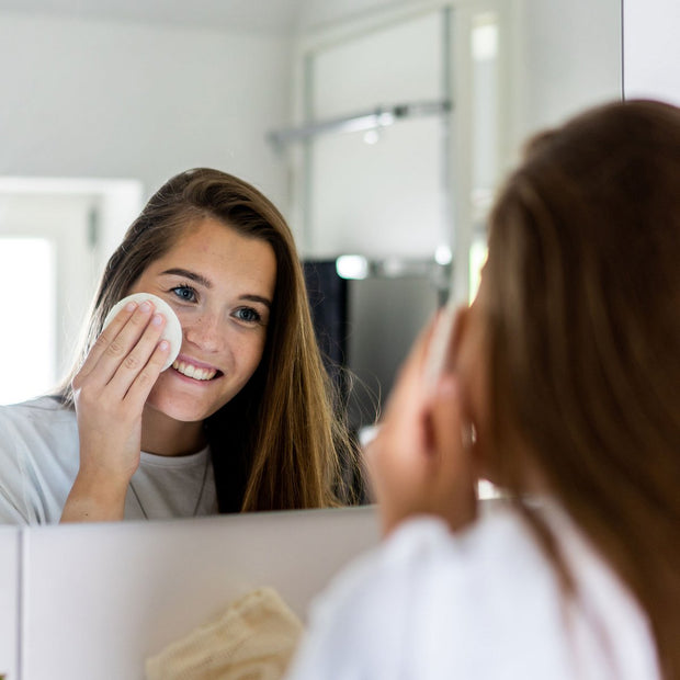 Jonge vrouw staat voor spiegel haar make-up eraf lachend eraf te halen met een wasbare, herbruikbaar wattenschijfje van Chinchilla.
